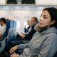 Mulher com bandagens no nariz, máscara e travesseiro de pescoço em assento azul de avião