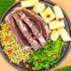 Cortes de carne crua, macaxeira, feijão fradinho, cheiro-verde e pimentas biquinho em travessa escura