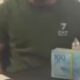Homem de camiseta verde, logo 7 EA7. Maço de notas de R$ 100 na mesa.