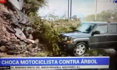 SUV cinza danificada por acidente, com arbustos e detritos, e texto 'CHOCA MOTOCICLISTA CONTRA ÁRBOL'