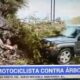 SUV cinza danificada por acidente, com arbustos e detritos, e texto 'CHOCA MOTOCICLISTA CONTRA ÁRBOL'