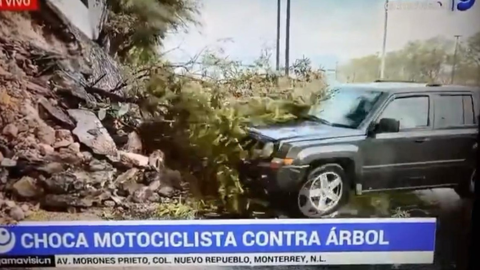 SUV cinza danificada por acidente, com arbustos e detritos, e texto 'CHOCA MOTOCICLISTA CONTRA ÁRBOL'