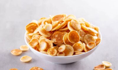 Tigela branca cheia de mini panquecas douradas e redondas sobre uma superfície cinza claro