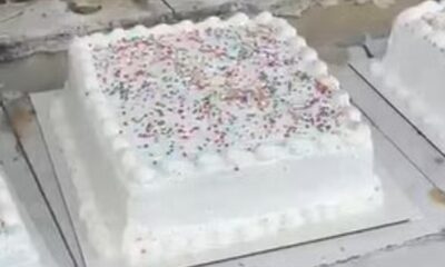 Bolo quadrado branco com glacê, granulados coloridos e esferas escuras na superfície