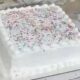 Bolo quadrado branco com glacê, granulados coloridos e esferas escuras na superfície