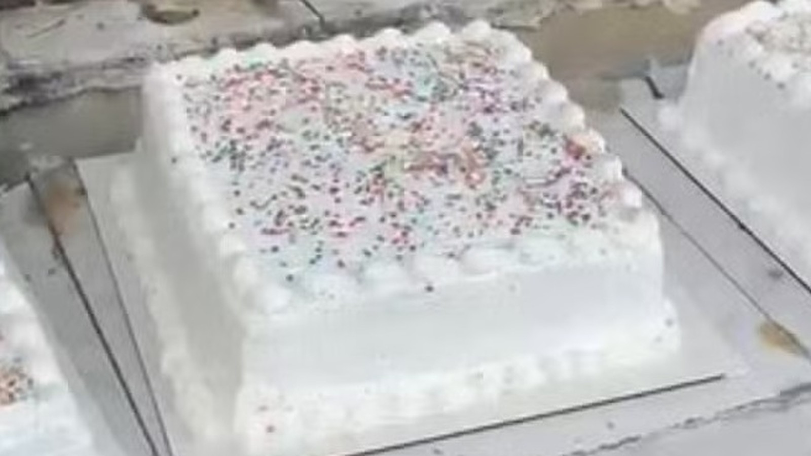 Bolo quadrado branco com glacê, granulados coloridos e esferas escuras na superfície