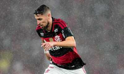 Homem barbudo com camisa do Flamengo, vermelho e preta, correndo sob chuva