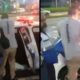 Homem com camiseta "CENOGRAFIA" sendo colocado em carro de polícia por agente "SEGURANÇA PRESENTE" à noite