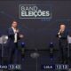 Flávio Bolsonaro apontando, Lula pensativo, em debate 'Band Eleições 2026', com intérprete de libras