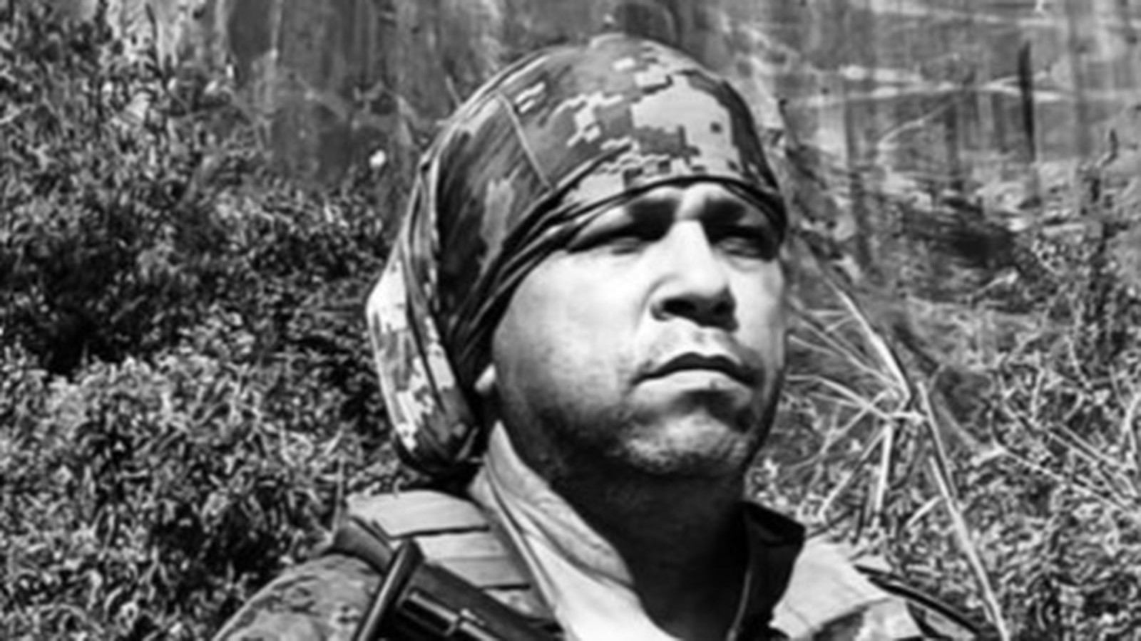 Retrato de homem em preto e branco com bandana camuflada e colete tático