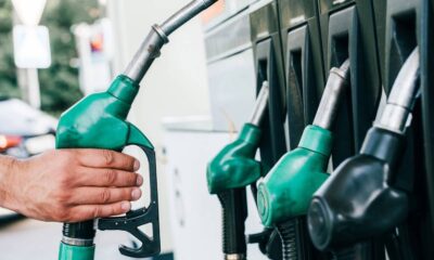 Mão de pessoa segura bico verde de bomba de combustível em posto de gasolina