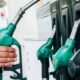 Mão de pessoa segura bico verde de bomba de combustível em posto de gasolina