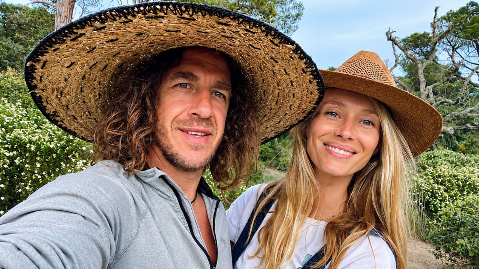 Carles Puyol e Vanesa Lorenzo sorrindo com chapéus de palha em meio à natureza