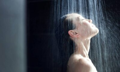 Mulher de perfil com os olhos fechados, tomando banho com água caindo sobre seu rosto e ombros