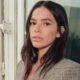 Bruna Marquezine, cabelo escuro, blazer xadrez, olhando à frente, com reflexo na janela