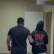 Agente escolta pessoa encapuzada em corredor de delegacia com placa de andares