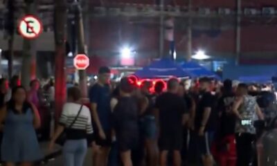 Multidão à noite em rua com luz vermelha, placas de proibido estacionar e pare
