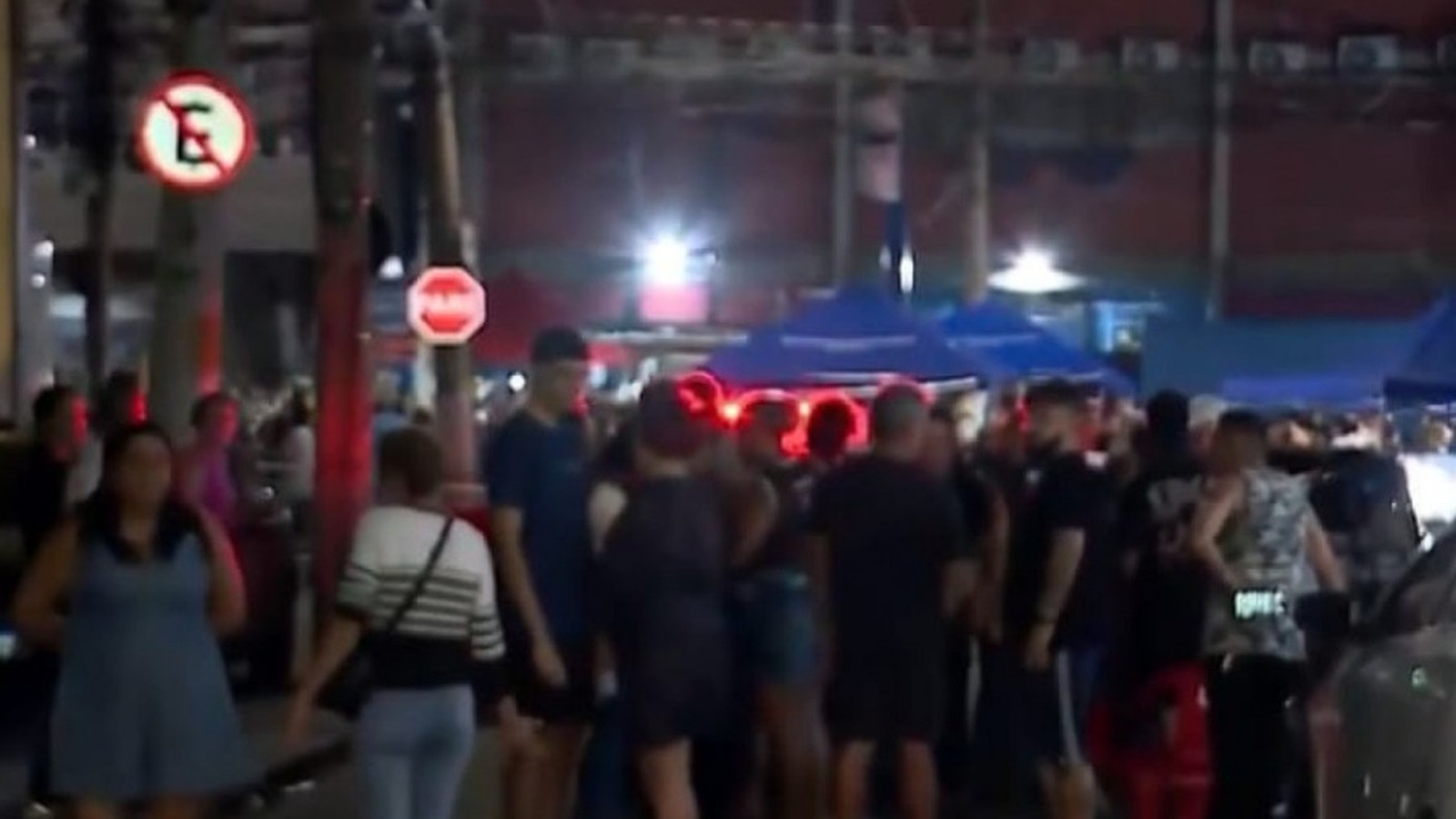 Multidão à noite em rua com luz vermelha, placas de proibido estacionar e pare