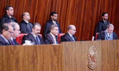 Ministros do Tribunal Superior Eleitoral, alguns sentados, alguns em pé, em sala de audiências formal
