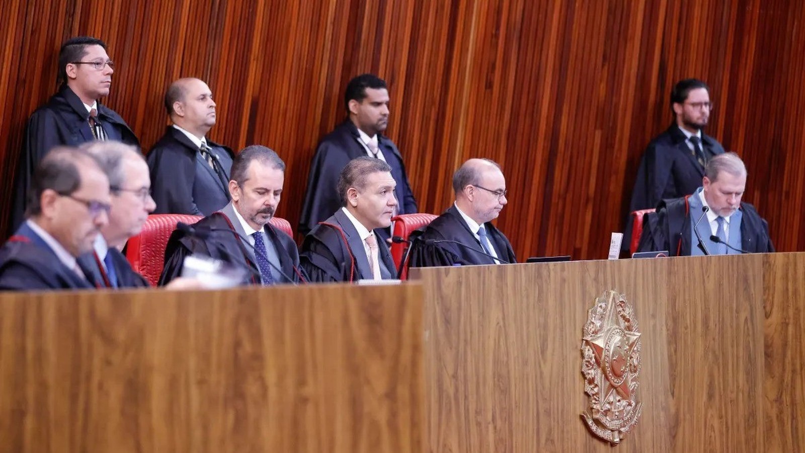 Ministros do Tribunal Superior Eleitoral, alguns sentados, alguns em pé, em sala de audiências formal