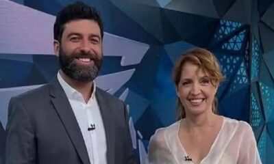 Rodrigo Carvalho e Poliana Abritta sorriem em estúdio de TV com fundo azul