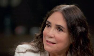 Mulher de meia-idade com cabelos escuros e grisalhos, usando blazer claro, olhando pensivemente