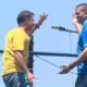 Flávio Bolsonaro (camisa amarela) e Douglas Ruas (camisa azul) acenam em trio elétrico sob céu azul