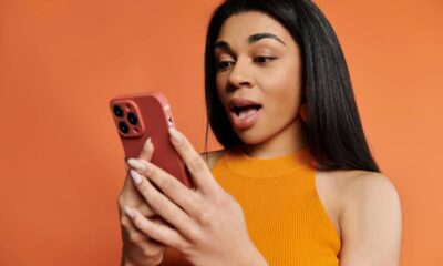 Mulher negra com expressão de surpresa olhando para o celular vermelho