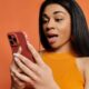 Mulher negra com expressão de surpresa olhando para o celular vermelho
