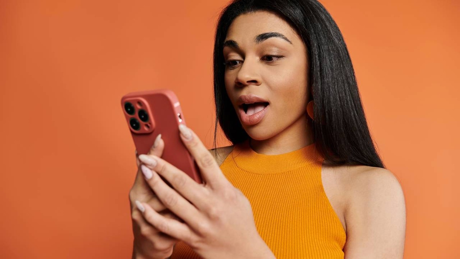 Mulher negra com expressão de surpresa olhando para o celular vermelho