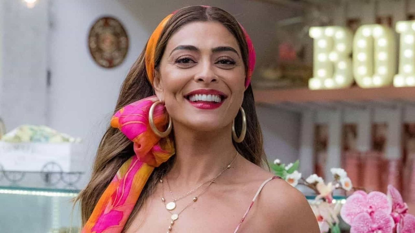 Juliana Paes sorrindo com lenço colorido na cabeça, brincos grandes e letras BOI ao fundo