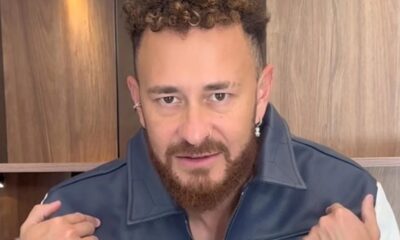 Homem com cabelo encaracolado e barba, vestindo jaqueta azul e branca, olhando para frente