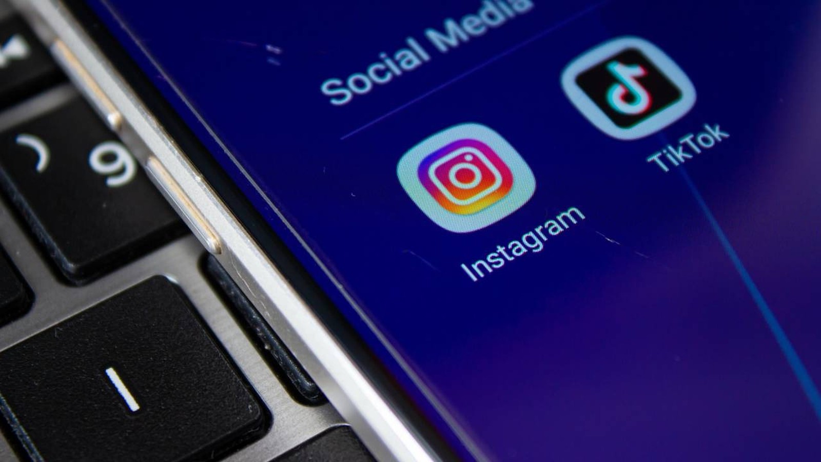 Smartphone screen displays Instagram and TikTok app icons on blue, beside a black keyboard