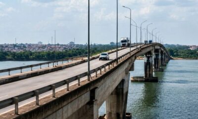Ponte de concreto sobre um rio com carros e caminhões, cidade no horizonte