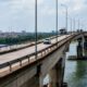 Ponte de concreto sobre um rio com carros e caminhões, cidade no horizonte