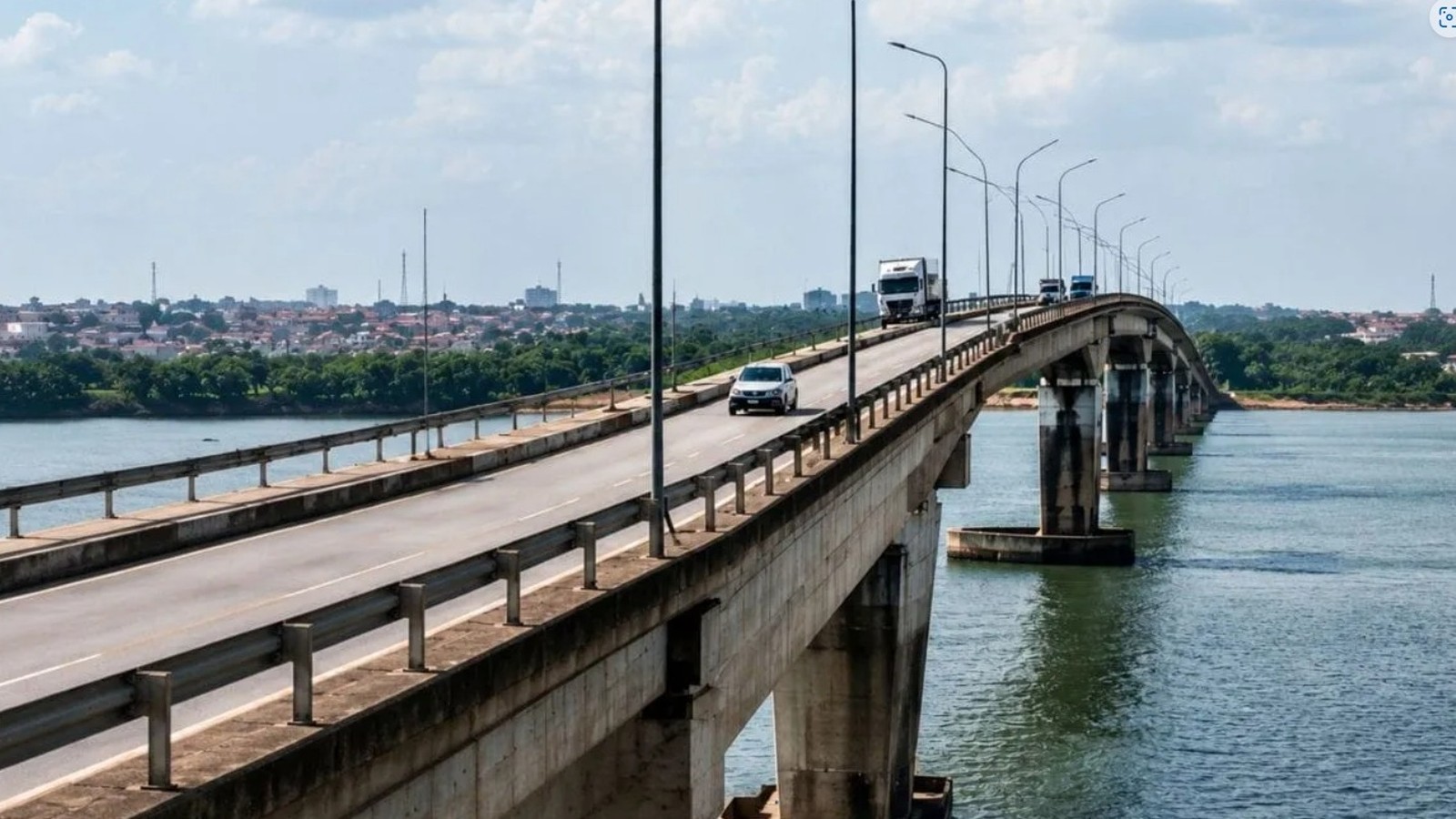 Ponte de concreto sobre um rio com carros e caminhões, cidade no horizonte
