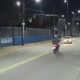 Rua noturna com moto, carro, postes de iluminação e muro azul com letreiro