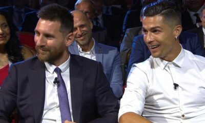 Lionel Messi e Cristiano Ronaldo sorrindo e sentados um ao lado do outro em evento