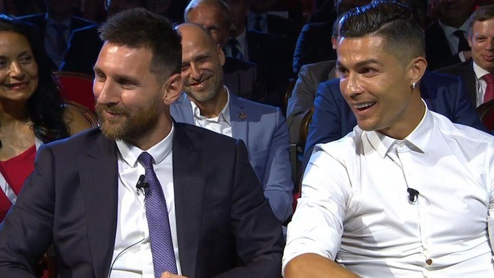 Lionel Messi e Cristiano Ronaldo sorrindo e sentados um ao lado do outro em evento