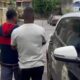 Dois homens de costas em rua, parte de carro de polícia com luzes azuis visível.