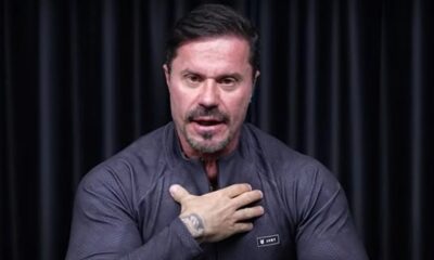 Renato Cariani, homem de barba, camisa escura com logo "ARMY", mão direita no peito, falando