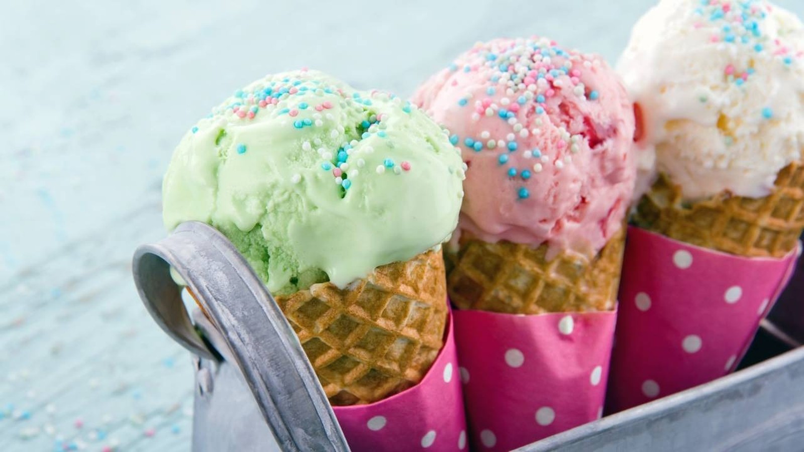 Três bolas de sorvete em casquinhas de waffle com granulados coloridos em bandeja metálica