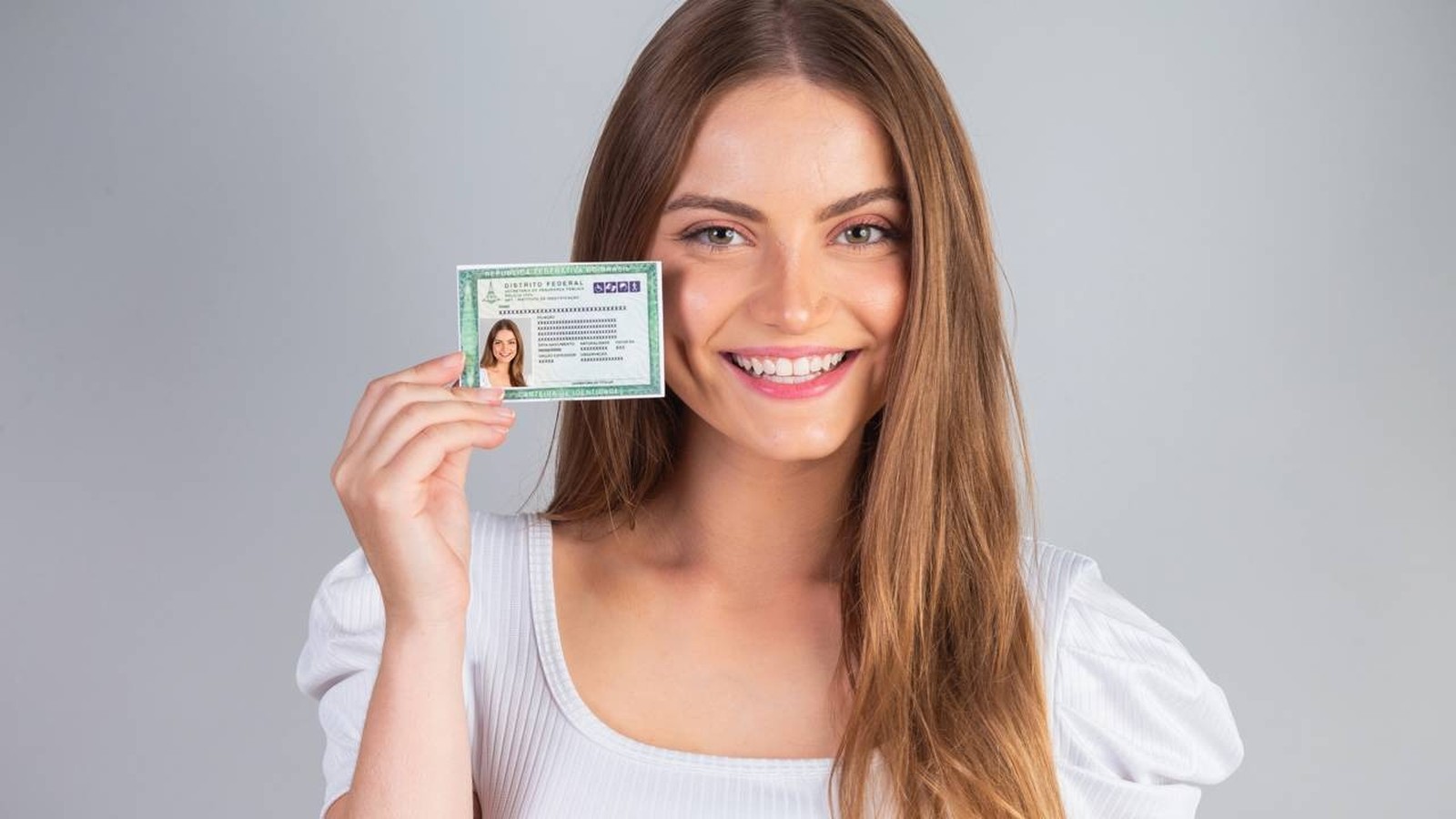 Mulher jovem sorridente segurando a nova Carteira de Identidade Nacional brasileira