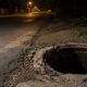 Vista em primeiro plano de bueiro aberto e danificado à noite em estrada escura com postes de luz