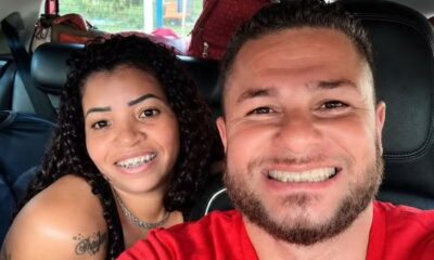 Casal sorridente em selfie no carro, homem com barba e mulher com aparelho dental
