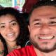 Casal sorridente em selfie no carro, homem com barba e mulher com aparelho dental