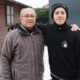 Homem idoso com óculos e homem jovem em quintal nevado, braços um sobre o outro