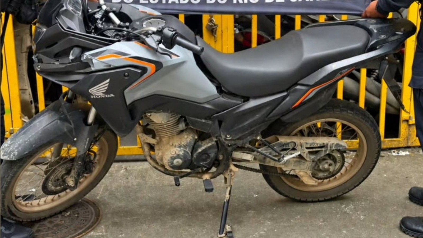 Motocicleta Honda XRE cinza e suja com detalhes em laranja, marca Honda visível
