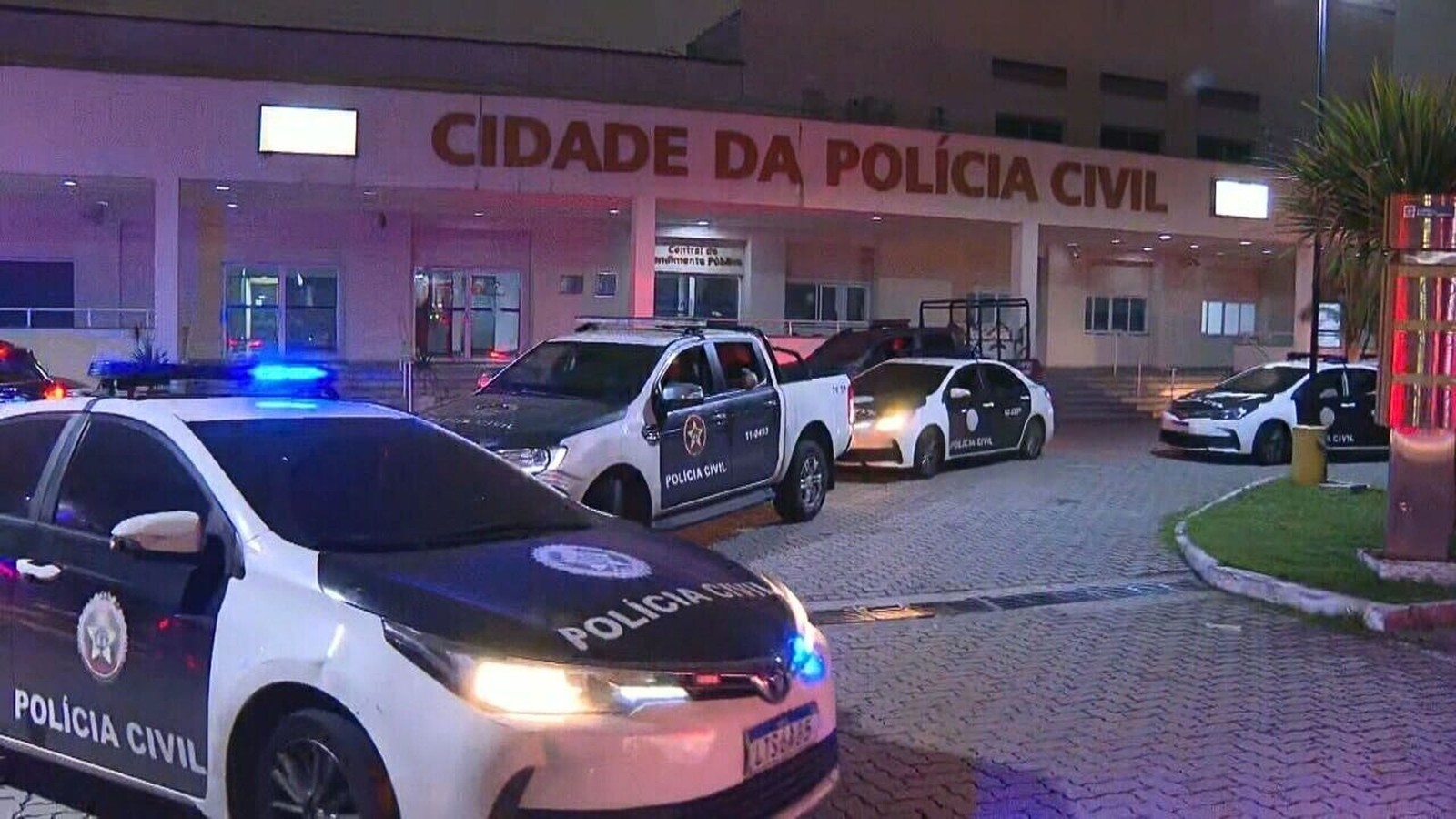 Viaturas da Polícia Civil com luzes acesas em frente à Cidade da Polícia à noite