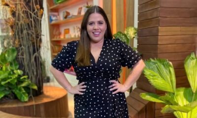 Tati Machado sorrindo, vestido preto de bolinhas brancas, mãos na cintura.